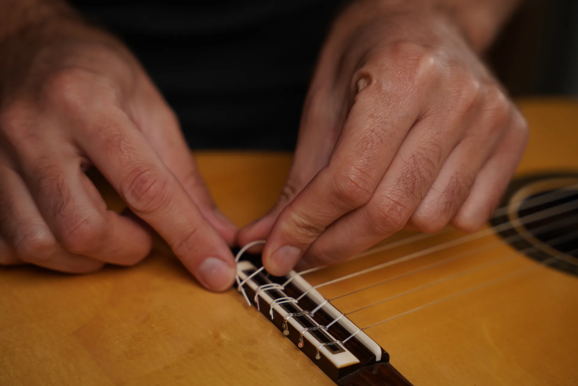 Press the loose end of the string firmly against the back face of the bridge — the most important point